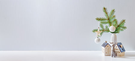 Christmas, New Year home decor. Empty white wall mock up with green fir branches in a vase, Christmas little house and deer on a white table. Mock up for display worksの写真素材