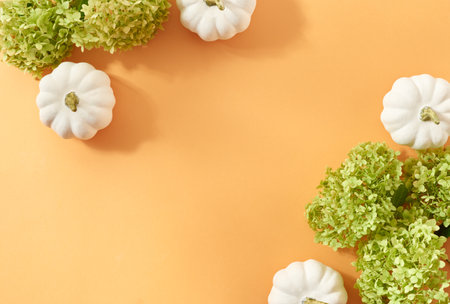 Flat lay autumn frame with green flowers and pumpkins on an orange backgroundの写真素材