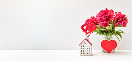 Red peonies in a vase and red heart, white house on a white table with copy space. Mock up for displaying works. Valentine's day holiday background conceptの写真素材