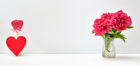 Red peonies in a vase and red heart on a white table with copy space. Mock up for displaying works. Valentine's day holiday background conceptの写真素材