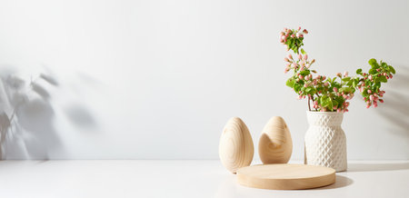 Empty round wooden podium for product presentation. Spring flowers in a vase and easter eggs on a light background.の写真素材