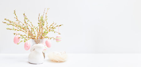 Branches with buds and green leaves in a vase, easter eggs on a white table. Easter background with copy spaceの写真素材