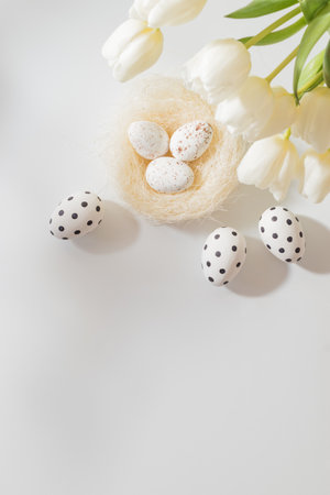 Flat lay easter composition with white tulips in a vase and easter eggs on a light backgroundの写真素材