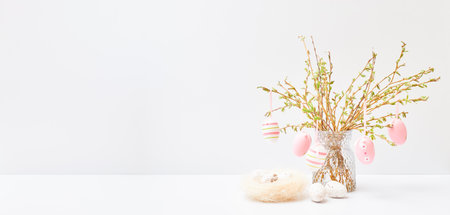 Branches with buds and green leaves in a vase, easter eggs on a white table. Easter background with copy spaceの写真素材