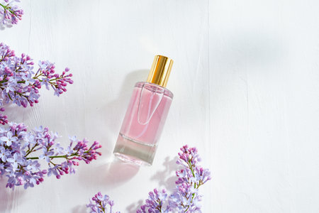 Pink glass perfume bottle and lilac branches on a white backgroundの写真素材