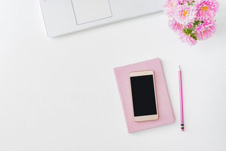 Flat lay home office desktop with laptop, pink flowers in a vase, notebook, office supplies on a light background. Top view mockup smartphone with blank screenの写真素材
