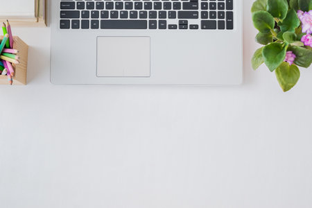 Flat lay home office desktop with laptop, flowers in a pot, book, office supplies on a light background. Top view banner background with copy spaceの写真素材