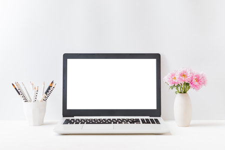 Office workspace with laptop mockup screen, books, pink flowers in a vase, supplies on a light background. Home interior or office backgroundの写真素材
