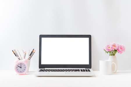Office workspace with laptop mockup screen, books, pink flowers in a vase, supplies on a light background. Home interior or office backgroundの写真素材