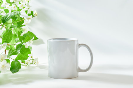 White mug mockup on a white background with sunlight and shadows of jasmine leaf flowersの写真素材