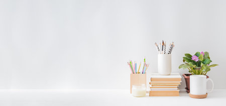 Home office, interior for bloggers workplace with copy space and flowers in a pot, supplies, books on a light background. Home interior or office backgroundの写真素材
