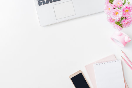 Flat lay home office desktop with laptop, pink flowers in a vase, notebook, smartphone, office supplies on a light background. Top view banner background with copy spaceの写真素材