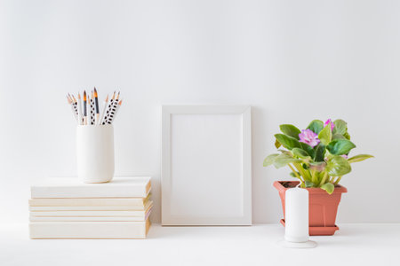 Mockup with a white frame, flowers in a pot on a light background. Empty poster frame mockup for presentation design, text, letteringの写真素材