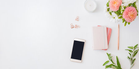 Flat lay home office desktop with notebook, flowers in a vase, office supplies on a light background. Top view mockup smartphone with blank screenの写真素材