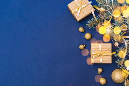 Flat lay christmas composition with golden gift box and christmas decorations, garland, fir branches on a blue background. Winter merry christmas holiday greeting cardの写真素材