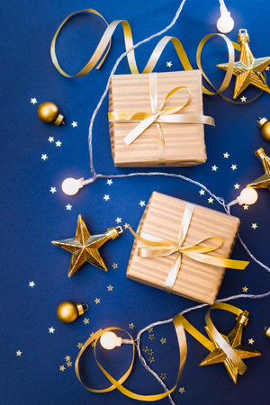 Flat lay christmas composition with golden gift box and christmas decorations, garland on a blue background. Winter merry christmas holiday greeting cardの写真素材