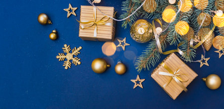 Flat lay christmas composition with golden gift box and christmas decorations, garland, fir branches on a blue background. Winter merry christmas holiday greeting cardの写真素材