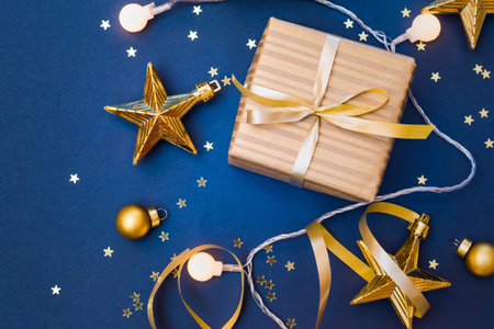 Flat lay christmas composition with golden gift box and christmas decorations, garland on a blue background. Winter merry christmas holiday greeting cardの写真素材
