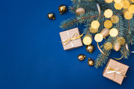 Flat lay christmas composition with golden gift box and christmas decorations, garland, fir branches on a blue background. Winter merry christmas holiday greeting cardの写真素材