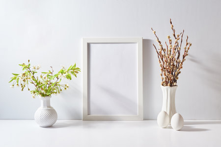 Mockup with a white frame and spring flowers in a vase, easter eggs on a light background. Empty poster frame mockup for presentation design, text, letteringの写真素材