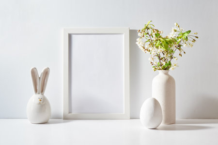 Mockup with a white frame and spring flowers in a vase, easter eggs on a light background. Empty poster frame mockup for presentation design, text, letteringの写真素材