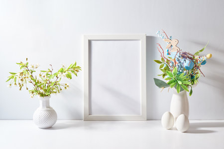 Mockup with a white frame and spring flowers in a vase, easter eggs on a light background. Empty poster frame mockup for presentation design, text, letteringの写真素材