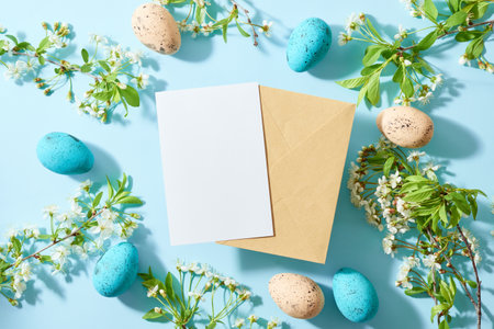 Mockup white greeting card and envelope, easter eggs with spring flowers on a blue backgroundの写真素材