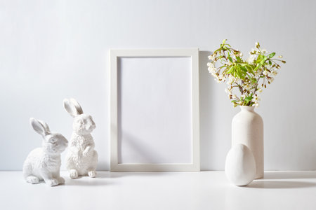 Mockup with a white frame and spring flowers in a vase, easter eggs on a light background. Empty poster frame mockup for presentation design, text, letteringの写真素材