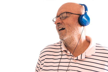 Happy old man in headphones singing with wall background, isolated with copyspace.の写真素材