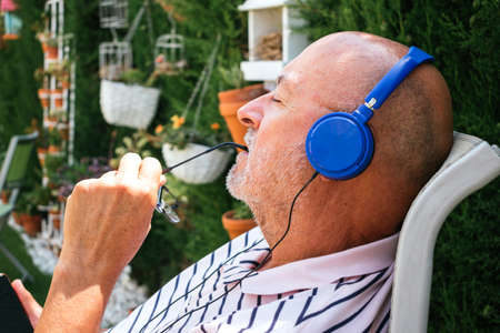 Closeup of a retired senior man listening music with closed eyes in relax time with blue headphones in a garden.の写真素材