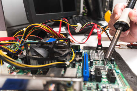 IT technician soldering a part of a computer motherboard in an officeの写真素材