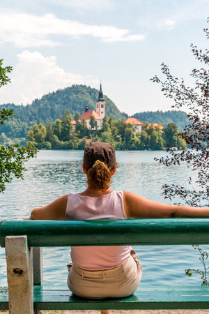 Woman tourist sitting on a bench with her back turned, looking out over Lake Bled in Slovenia.の写真素材