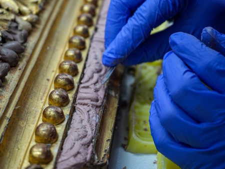 Detail of the hands of a professional man using a scalpel with latex gloves to restore a gold leaf...