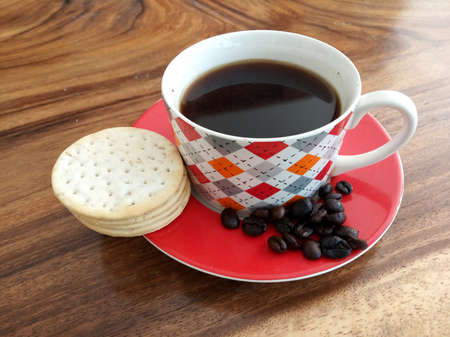 A cup of black morning coffee with cookies, raw coffee beans on wooden table. Fresh morning coffee drink concept. Copy space.の写真素材