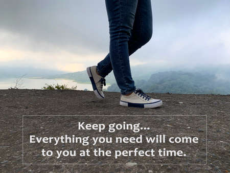 Inspirational quote - Keep going. Everything you need will come to you at the perfect time. With feet of young woman walking on the street on background of top foggy mountain with gloomy sky.の写真素材