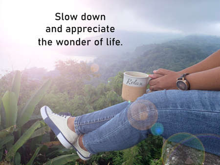 Inspirational quote - Slow down and appreciate the wonder of life. With person sitting holding coffee or tea cup with relax legs enjoying nature view in the edge of top of mountain. Grateful concept.の写真素材
