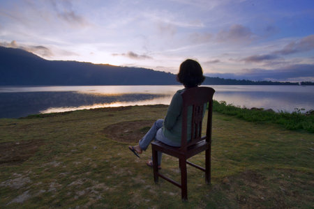 Relax person sitting on a chair enjoying the lake morning view at sunrise. woman siting alone on chair in silence looking at the tranquil morning view in the lake. Be still concept.の写真素材