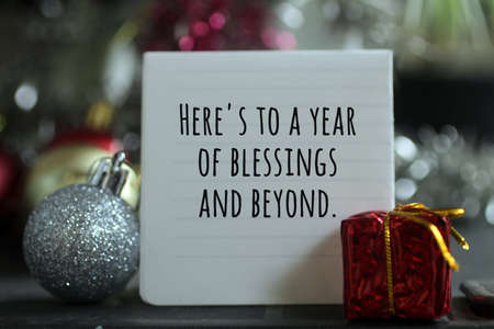 New Year inspirational quote - Here's to a year of blessings and beyond. With red Christmas gift box and white ball Christmas decorations background. New year wishes concept.の写真素材