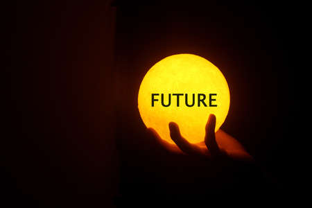 Person holding future yellow ball lamp in hand in the dark. Man carry light lantern with text - FUTURE. Hope concepts. Your future life in your hand. Business success and happiness concepts.の写真素材