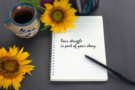 Life story inspirational quote - Your struggle is part of your story. Text on notebook with pen, coffee cup and sunflowers decoration on the gray table background. Life journey.の写真素材