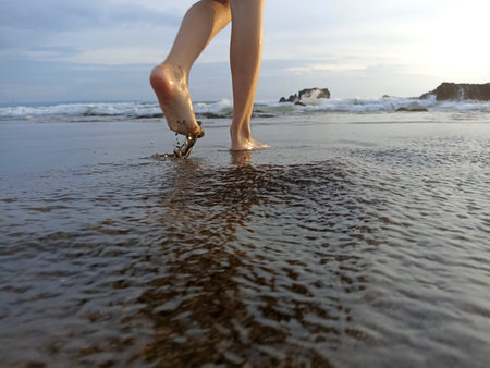 Barefoot of young woman walking on black sand beach. Relax feet or legs of a girl taking a walk on beach in the morning.の写真素材