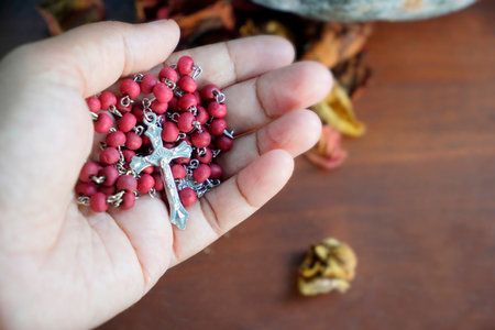christian cross with red beads in hand on a wooden table.の写真素材