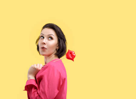 European woman on a yellow background in bright clothes. Surprised keeps big red lips near faceの写真素材
