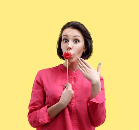 European woman on a yellow background in bright clothes. Surprised shows hand on big red lips....