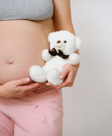 Caucasian mother holds a white Teddy bear near her belly during pregnancy. The concept of happy...