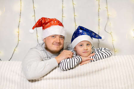 happy family father and child little daughter sitting on the sofa in Santa hats waiting for the Christmas miracle and new year's giftsの写真素材
