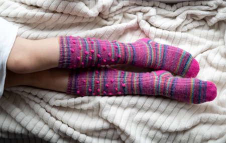 The legs of a young girl in lilac knitted socks-knee socks lying on a white soft bedspread. Cozy handmade knitted thingsの写真素材