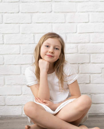 Portrait of a happy child - a little blonde girl 8-9-10 years old, against the background of an empty white brick wall, dressed in rabbit ears, holding hands in the shape of a heart. Medium planの写真素材