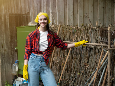 A young woman is an agricultural worker working with flowers in a greenhouse. a girl in yellow gloves, shirt and jeans on the background of a plantation. The concept of natural gardeningの写真素材