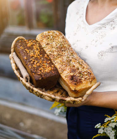 Baker's hands holding loaves of homemade bread in a wooden basket against the background of grass. Yeast-free wheat and rye bread with sourdough. Family bakery. The concept of eco food and productsの写真素材